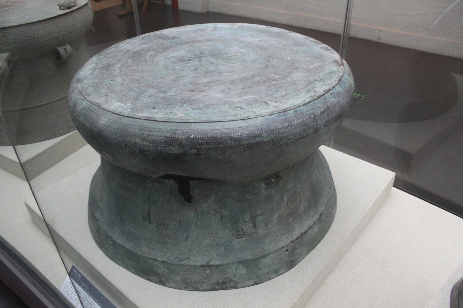 Un grand tambour de bronze au décor concentrique se tient dans une vitrine de musée.
