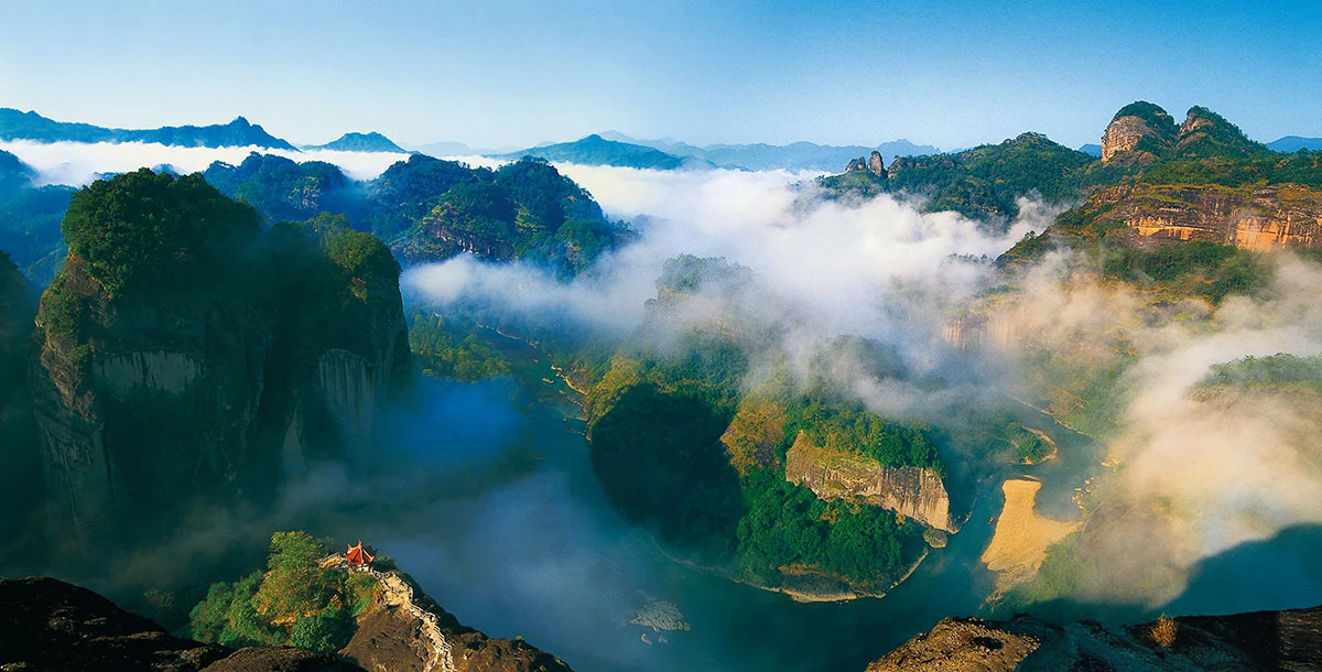 Nubes bajas cruzan una vista elevada de un recodo del río y escarpadas formaciones rocosas arboladas.