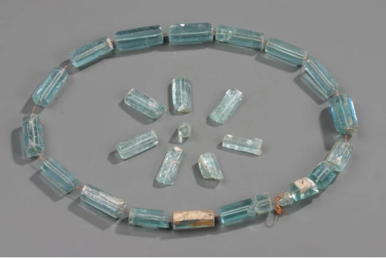 Des parures en verre bleu pâle de section hexagonale, disposées en anneau et en groupe épars.
