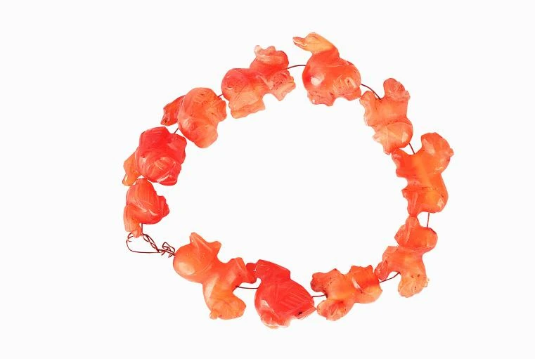 Des ornements animaliers en agate orange sont disposés sur un fil rouge, sur fond blanc.