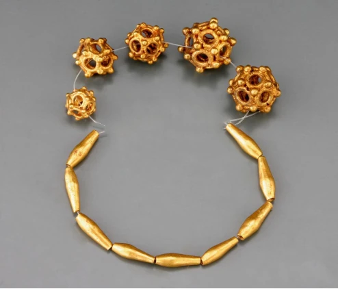 Des perles en or ajourées et des parures allongées en or, disposées sur un fond gris.
