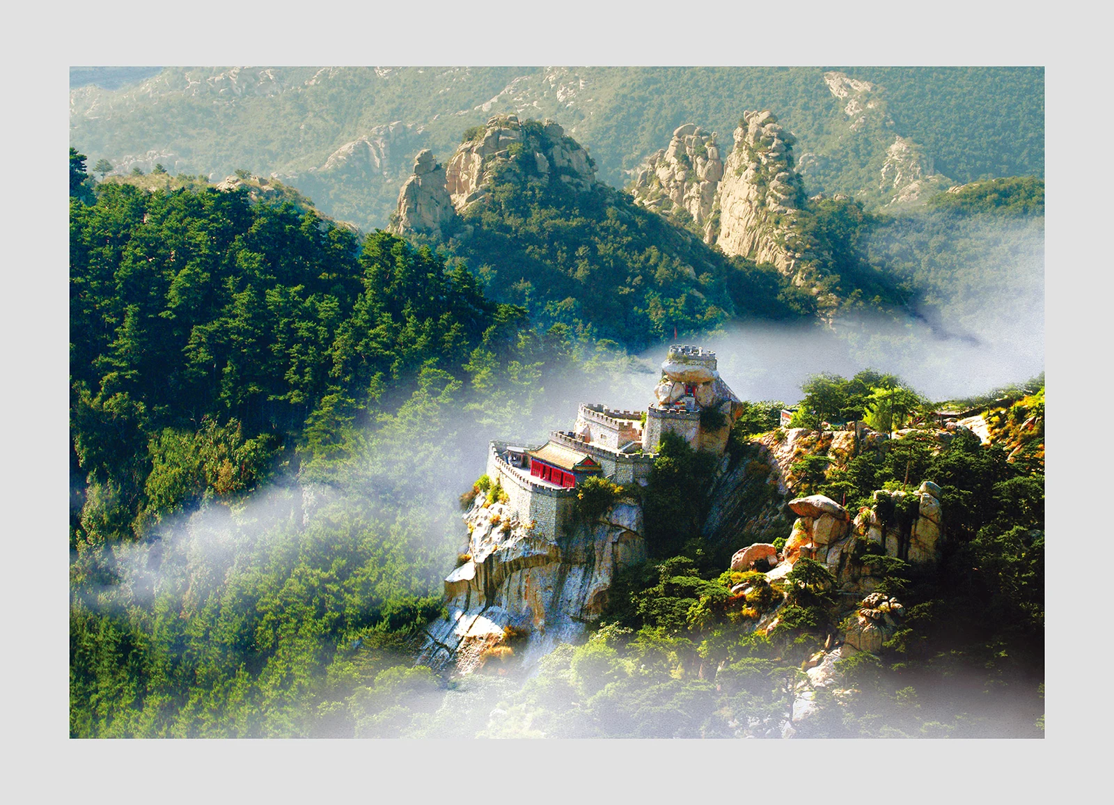 Un petit bâtiment rouge et des terrasses de pierre s’accrochent à un affleurement rocheux, au milieu de sommets verts et de brume.