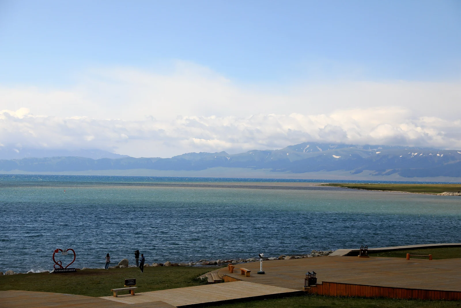 The shore of Sayram Lake: open water, a boardwalk and the snow-streaked mountains beyond.