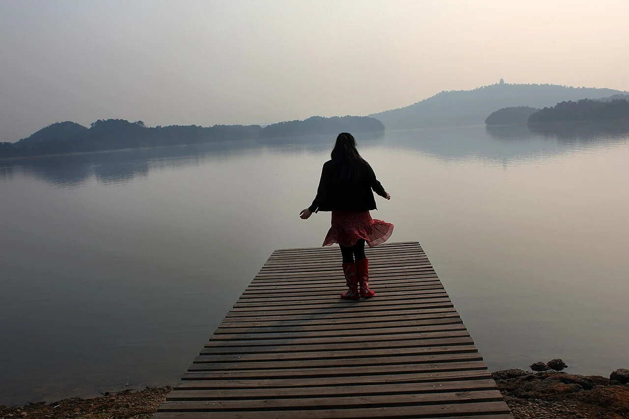 Una persona está en un muelle de madera frente a islas bajas y boscosas del embalse Fairy Lake, en Xinyu.