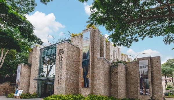 Um edifício contemporâneo dedicado à arte do órgão, revestido de pedra e à sombra de árvores frondosas.