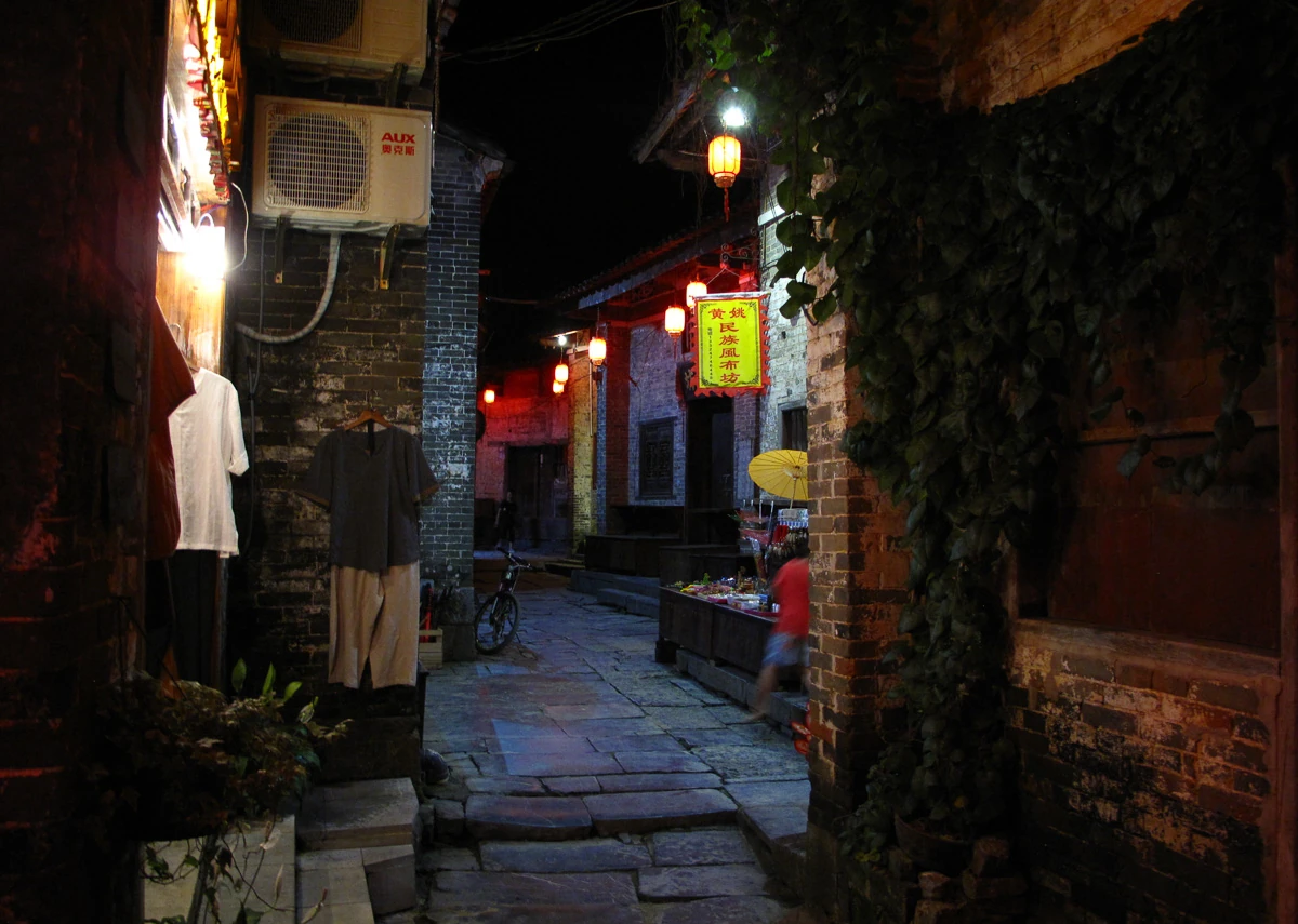 Warm lights and lanterns illuminate a stone-paved lane in Huangyao after dark.