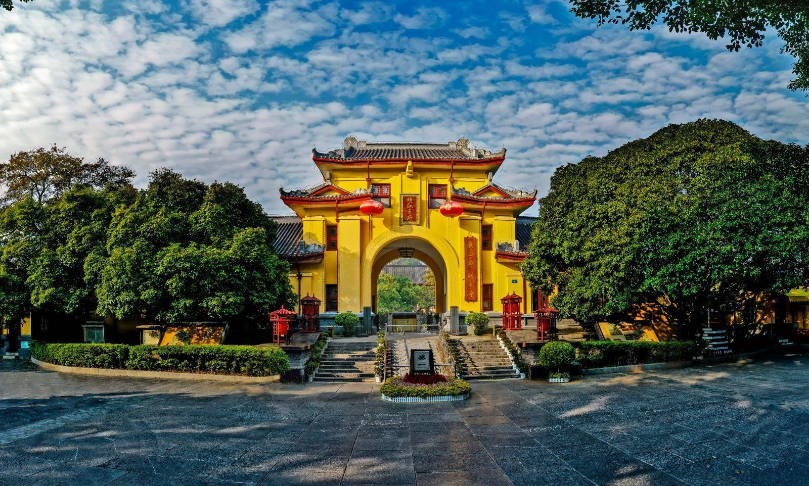 Yellow entrance gate at Jingjiang Princes’ City framed by trees and a blue sky.