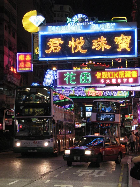 Neonschilder leuchten über Doppeldeckerbussen auf einer Straße in Hongkong.