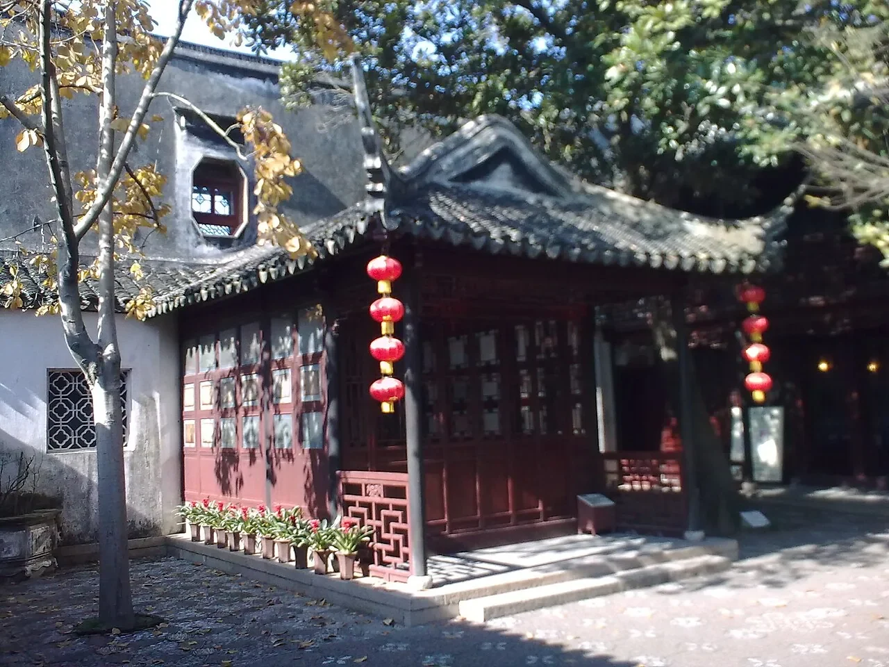 Un pavillon de bois rouge au toit courbe, orné de lanternes, dans le jardin Tuisi.