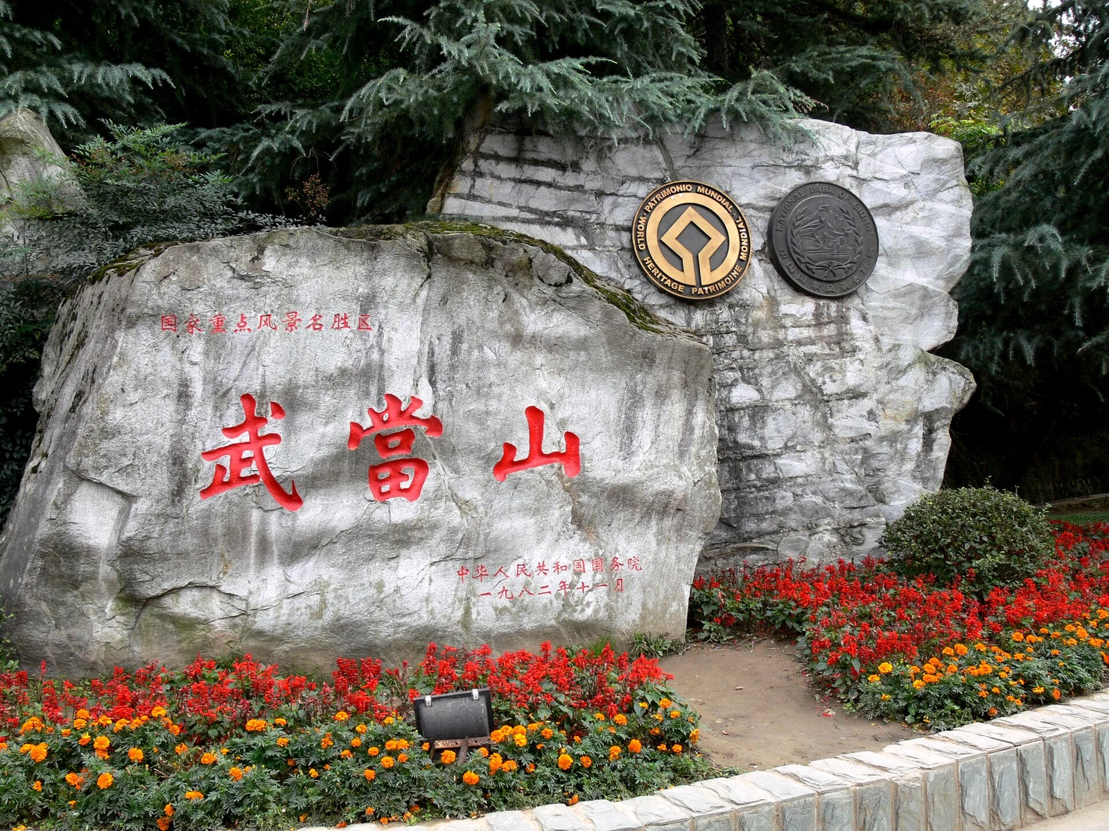 Le bloc gravé de l'entrée du mont Wudang, ses caractères rouges sur la pierre grise, l'emblème du patrimoine mondial dans les parterres.