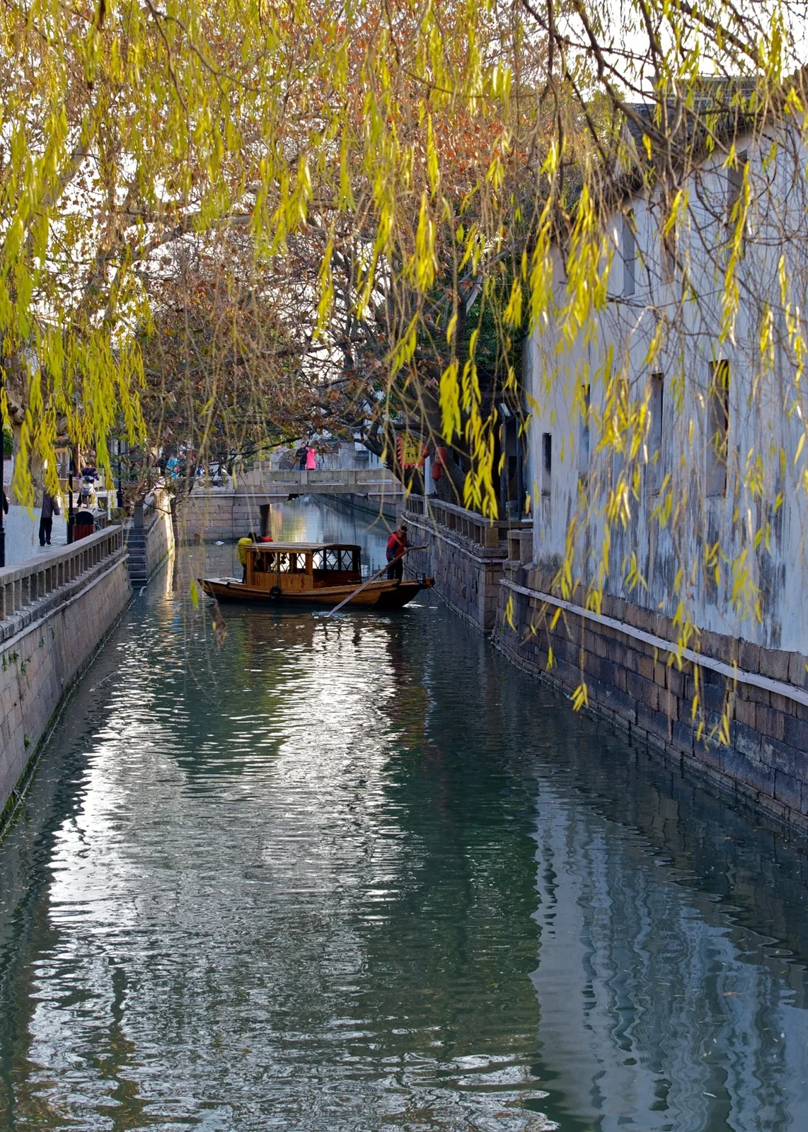 Une embarcation couverte sur un étroit canal de la rue Pingjiang, sous des branches de saule retombantes.