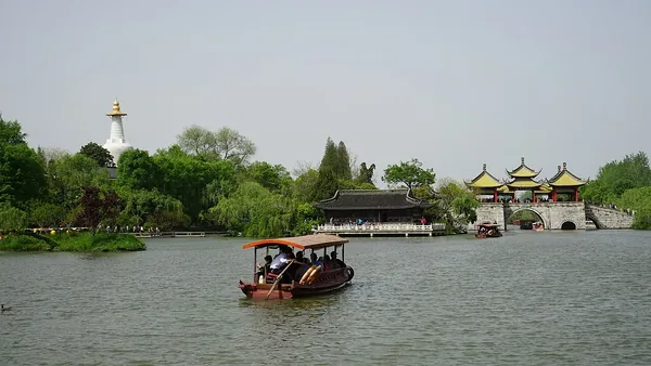 A covered boat crosses Slender West Lake with the Five-Pavilion Bridge and white pagoda beyond.