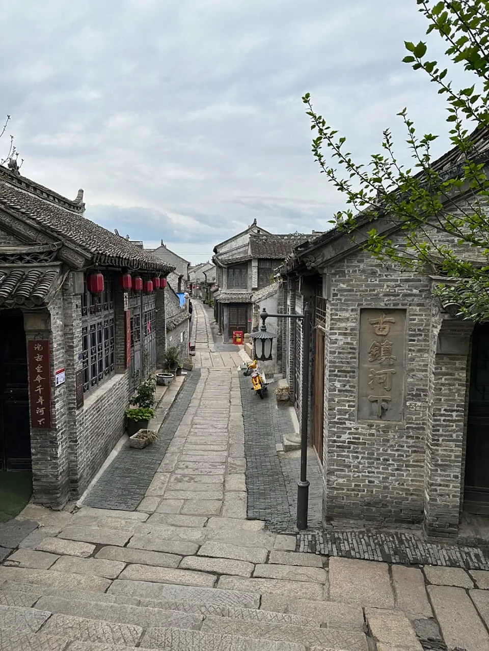 A narrow paved lane between gray-brick buildings near the south entrance of Hexia Ancient Town.