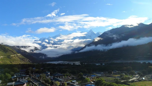 Namcha Barwa über einer Talsiedlung unter einem Wolkenband