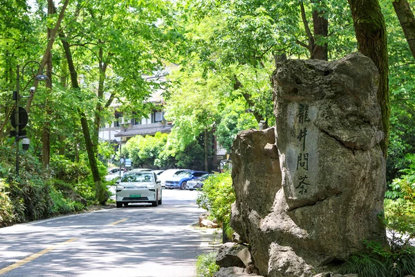 Un marcador de piedra con la inscripción «Longjing wencha» está junto a un camino arbolado de la aldea.