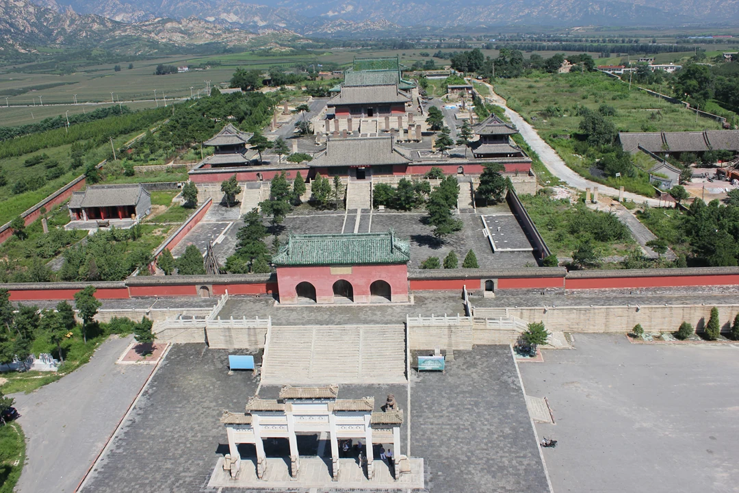A stone archway, red gateway, courtyards and tiled halls align in front of a rocky mountain range.