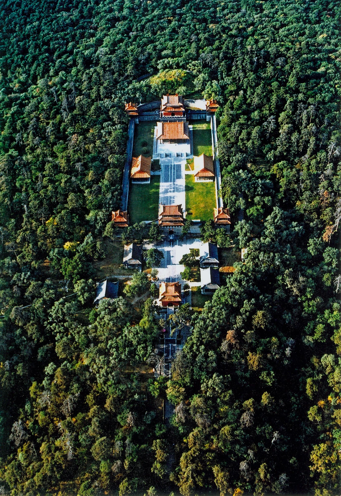 Una larga línea de patios, torres y escaleras atraviesa un bosque denso, vista desde gran altura.