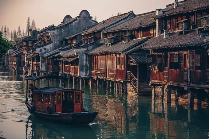 Timber rooms project over Wuzhen's canal as a covered boat passes below.