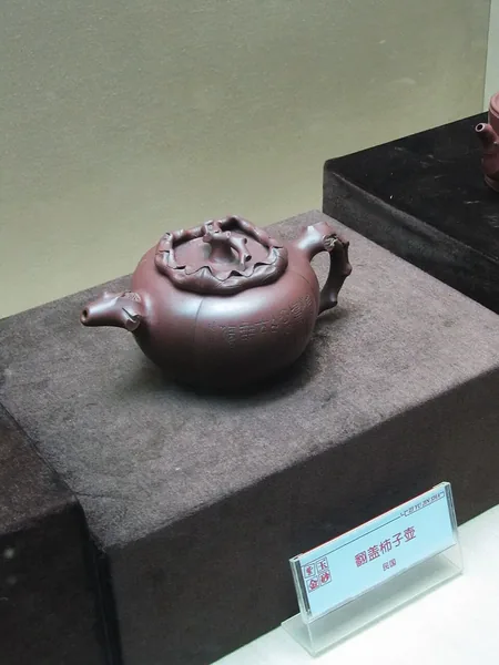 深色博物館展座上，一把壺蓋帶雕塑裝飾的紅褐色宜興茶壺。