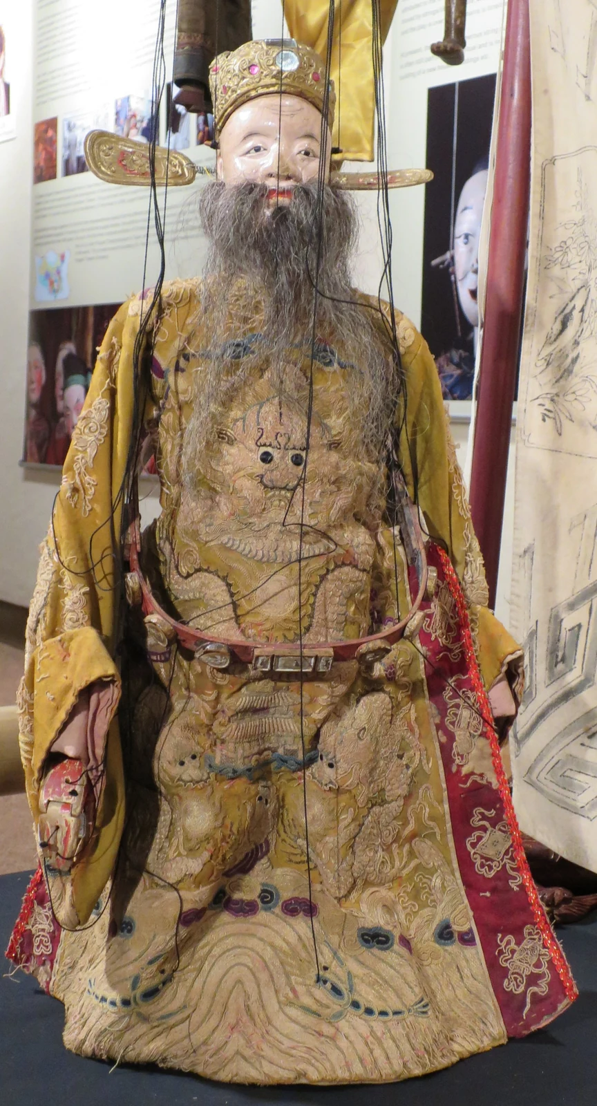 Eine geschnitzte Figur in bestickter Robe mit langem Bart, aufrecht ausgestellt.