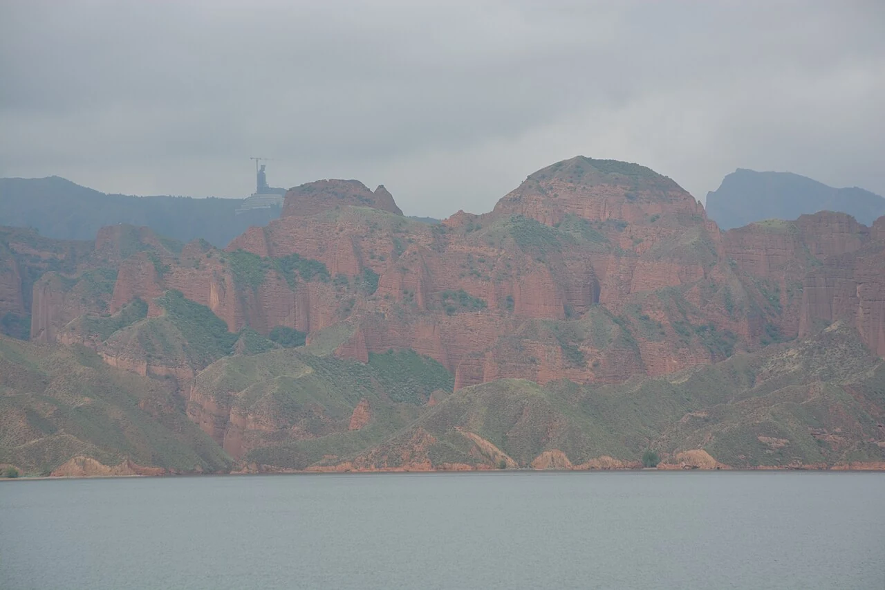 Kanbula’s red hills beside the reservoir, photographed in May 2026.