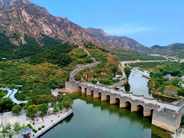 石牆藉拱形孔口跨河，向綠色岩山坡上延伸。