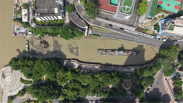 Вид сверху на длинный заполненный водой док с судном, деревьями и окружающими дорогами.