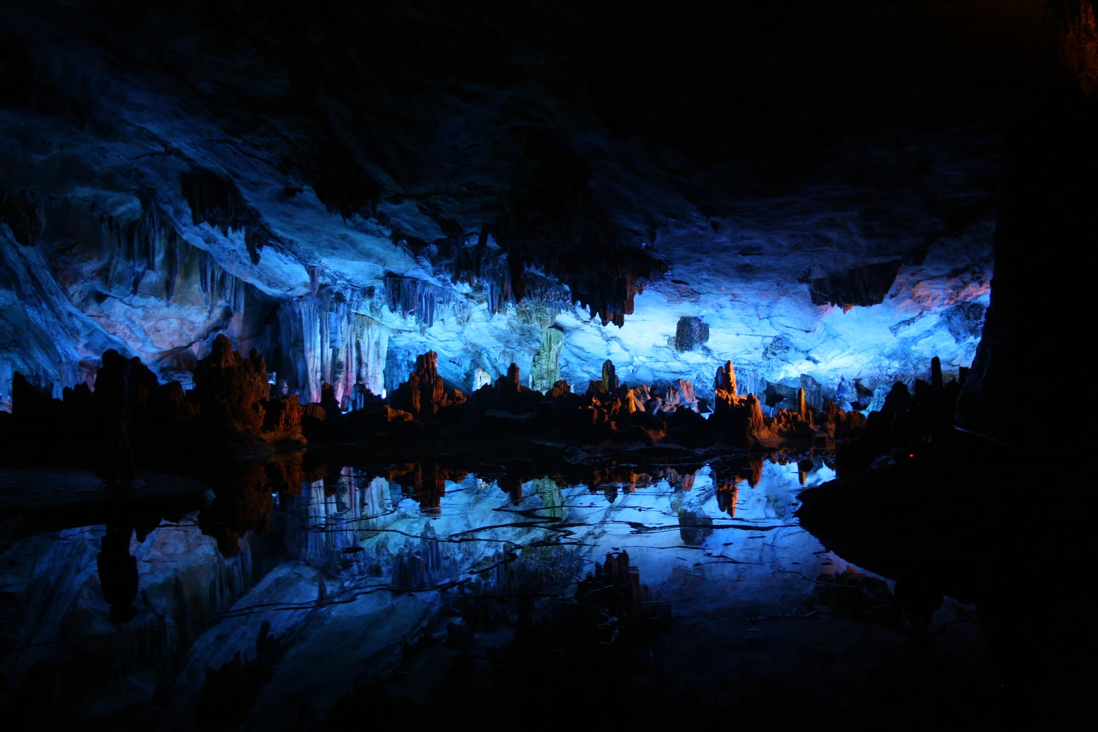 Luz artificial azul ilumina formaciones calizas reflejadas en una poza de una cueva.