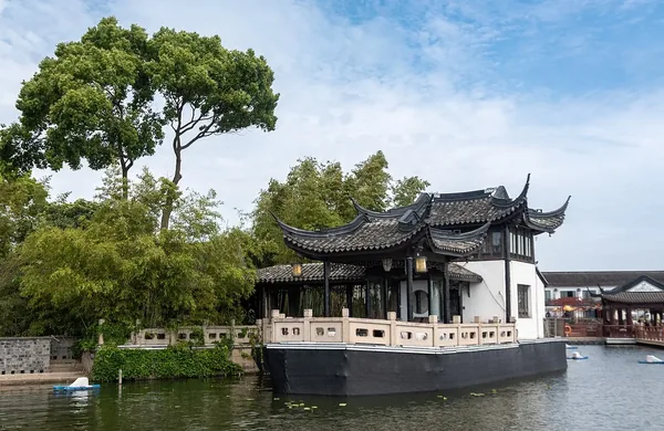 A curved-roof waterside pavilion beside a tree and reflective water in Zhouzhuang.