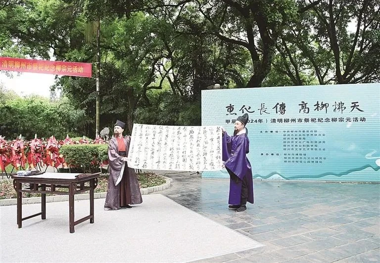 Two participants in ceremonial robes display calligraphy during a memorial ceremony.