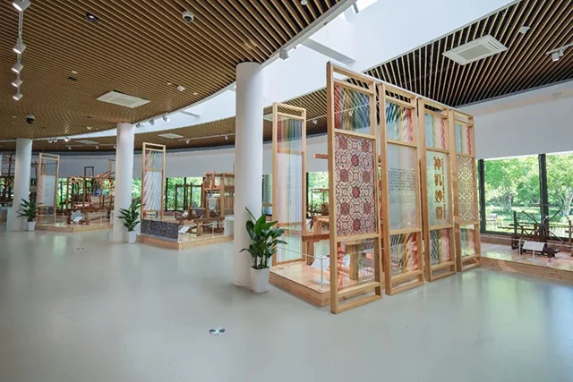 明亮的博物館展廳中，木製展架上陳列著紋樣織物，裡面還可看到織機。