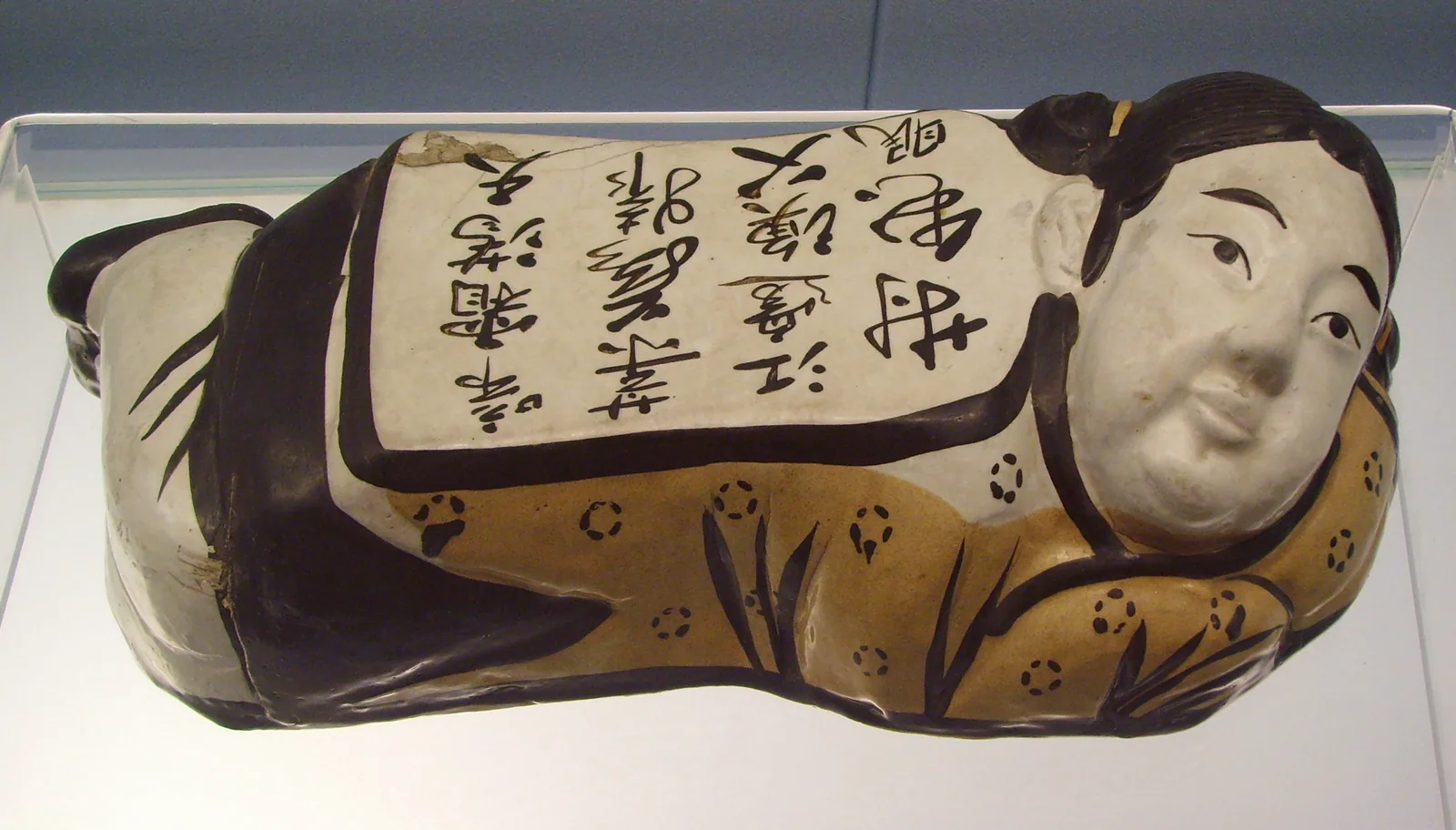 Almohada en forma de niño del horno de Cizhou, dinastía Jin, pintada en negro sobre engobe blanco.