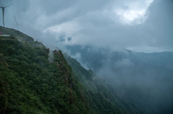 Jiugong-Berg: bewaldete Grate über den Wolken, mit einer Windkraftanlage auf dem Kamm.